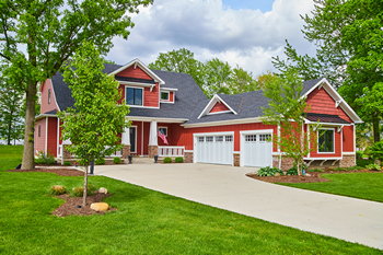A large red house with a driveway and a tree in the front yard, showcasing a welcoming suburban scene.