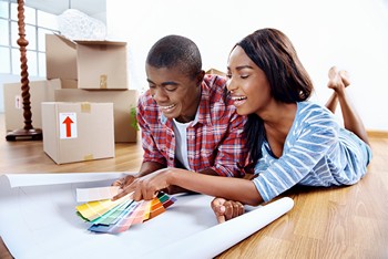 A young couple relaxes on the floor, examining a colorful paint sample together.