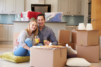 A couple enjoys pizza on the floor, surrounded by moving boxes, creating a relaxed atmosphere.